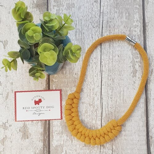 mustard necklace flat lay with green plant and business card next to the necklace