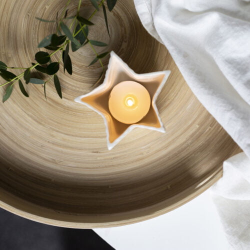 Star porcelain tea light holder, lit on a wooden tray.