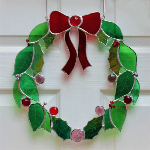Decorative stained glass wreath with a large red bow, green leaves and a variety of coloured beads and baubles