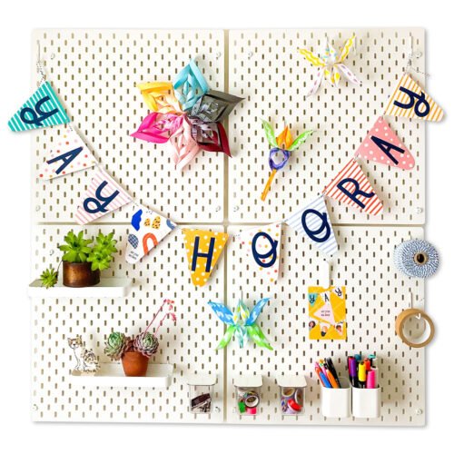 colourful paper bunting with the words Yay Hooray hanging on white pegboard with an assortment of colourful decorations, plants and stationery items