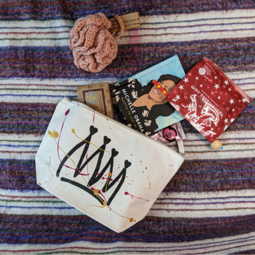 A flatlay of a zipped make-up pouch with a crown print. Cosmetic items are spilling out.
