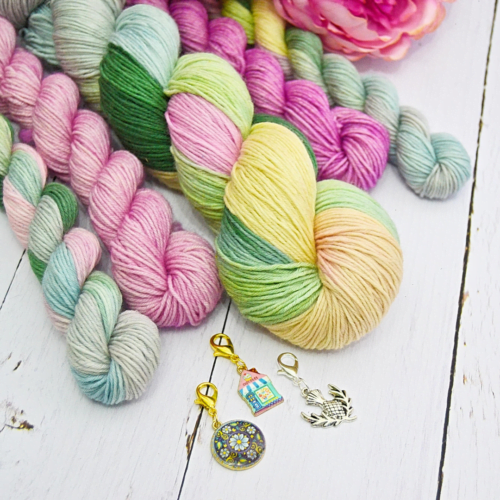 Multiple skeins of hand-dyed wool and three stitch markers on table