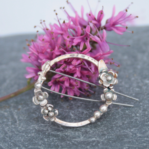 Sterling silver botanical brooch lying against a pink flower