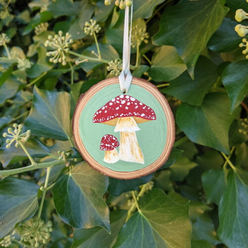 Hand Painted Mushroom Wood Slice Decoration against a green leafy background