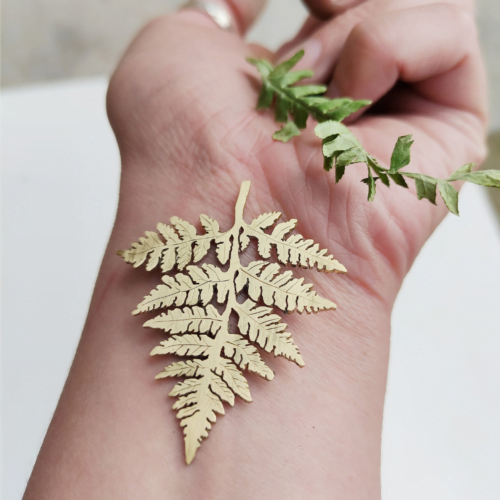 A delicate brass fern rests on the inside of a wrist