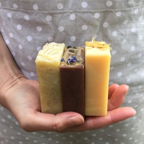 3 colourful bars of soap in hand against a spotty apron