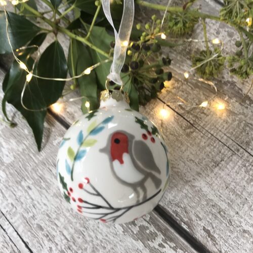 Hand painted bauble featuring robin sitting on a branch with red berries and hand painted holly leaves and branches in a fresh green and aqua colour