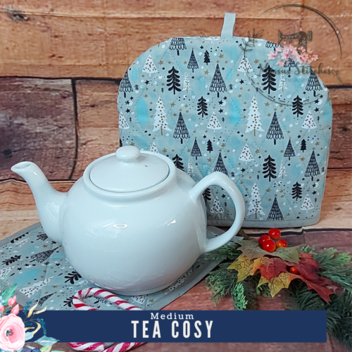 Christmas trees in blue, white and black on grey backing Tea cosy, sitting behind a white teapot resting on a matching pot rest