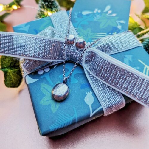 Picture shows a botanical wrapped gift box with sparkly silver ribbon. Draped over the box is a pair of round pebble shaped silver stud earrings with a small pebble/ nugget pendant on a silver belcher chain. All made by Arty Jeweller.